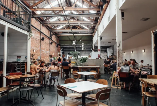 Interior kafe bergaya industrial dengan rangka atap baja dan dinding bata ekspos yang ramai pengunjung